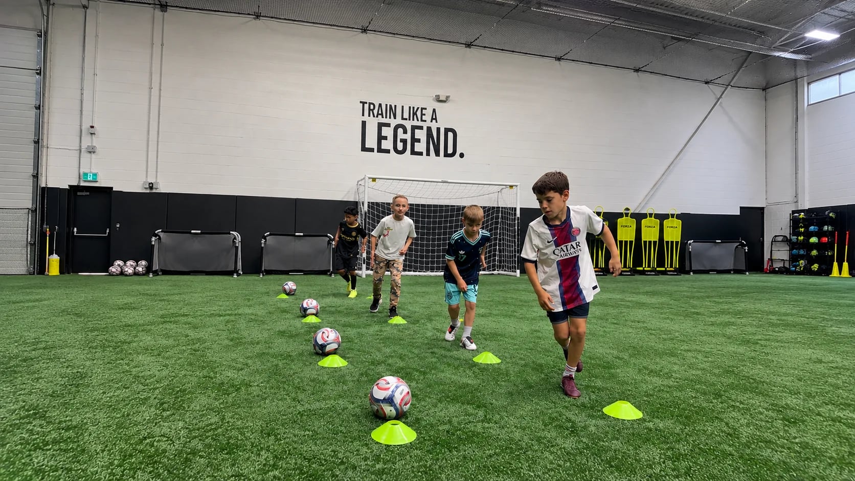 Young players dribbling soccer balls through cones on the indoor turf at Legends Training Factory.