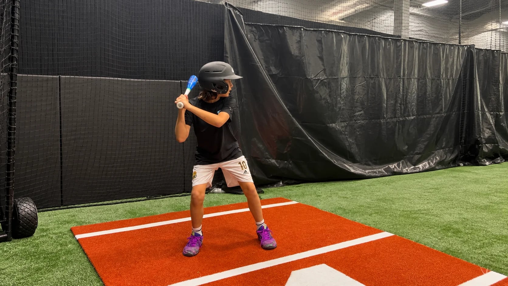 A young batter in a helmet hitting off a tee in the batting cage at Legends Training Factory.